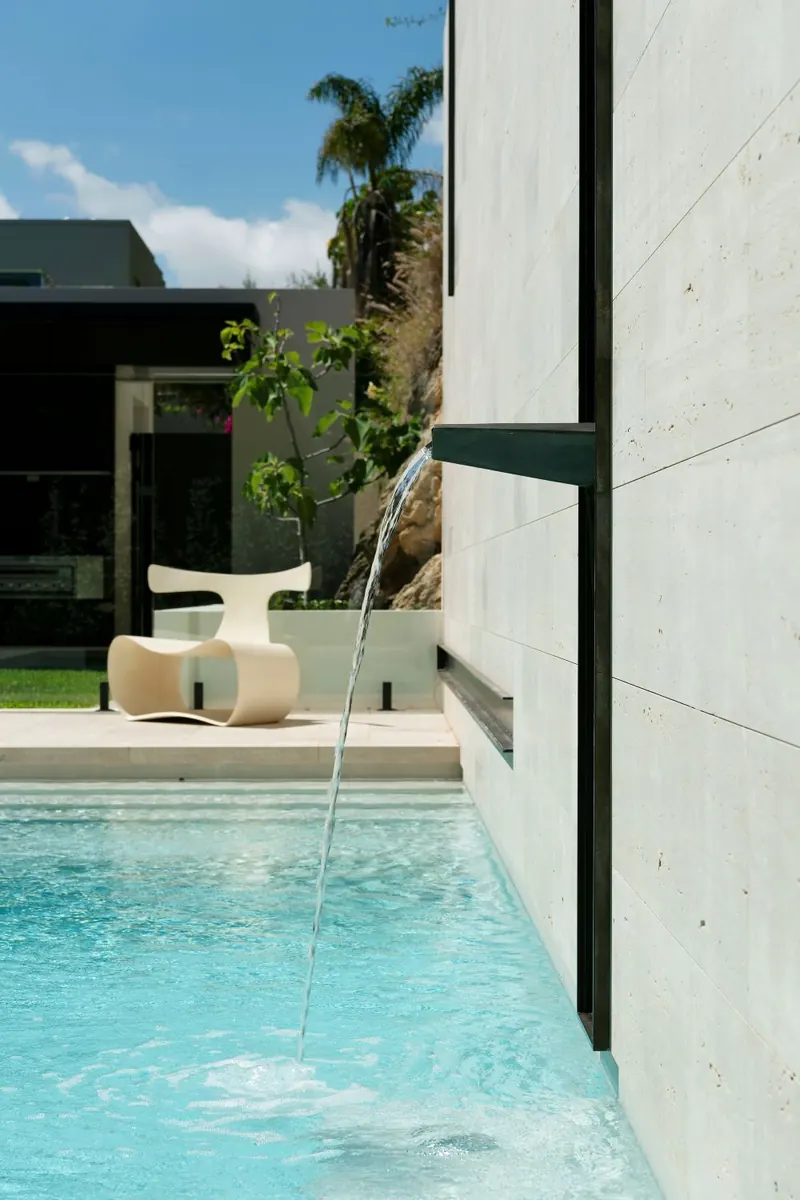 Water spout feeding the pool beside an off-form concrete wall
